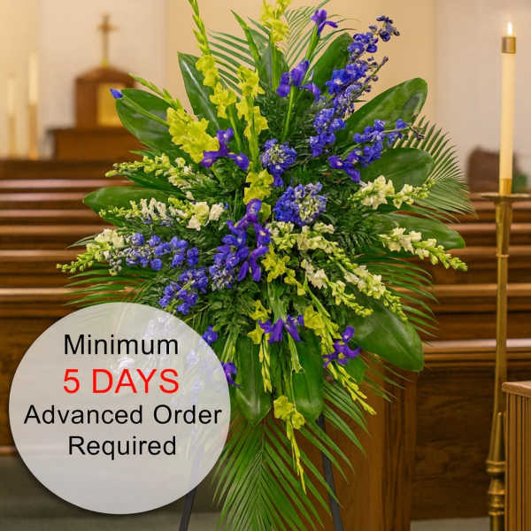Tall standing spray of blue and yellow flowers with lush foliage on an easel in a church.