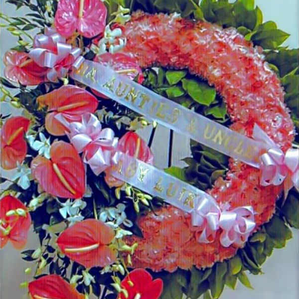 Funeral wreath with pink flowers and red tropical blooms on green leaves with white ribbons