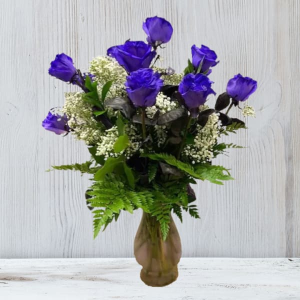 Arrangement of vivid purple roses with white filler flowers in a brown glass vase
