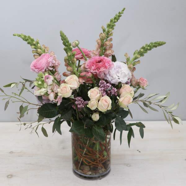 Tall pastel pink and white flower arrangement with roses and ranunculus in a clear glass vase.