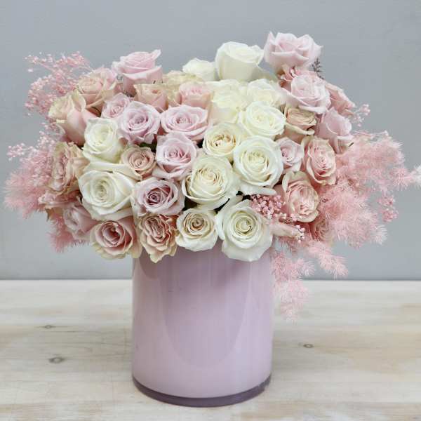 Tight arrangement of cream and blush roses in a pastel pink cylinder vase