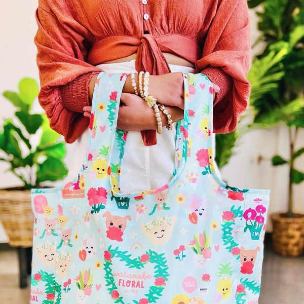 Pastel blue reusable tote bag with colorful cartoon flowers and characters held in front of a person.
