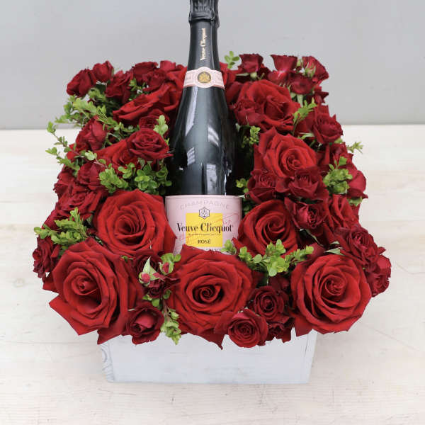 Bottle of rosé champagne surrounded by red roses in a white wooden box
