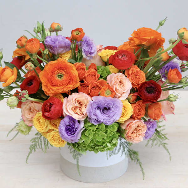 Low white vase filled with bright orange, red, yellow, and purple flowers in a wide arrangement