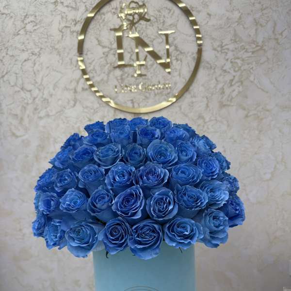 Dense arrangement of vivid blue roses in a light blue hatbox-style container.