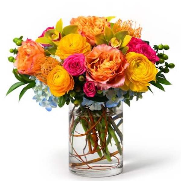 Bright orange, yellow, and pink flower arrangement in a clear glass cylinder vase with submerged branches.