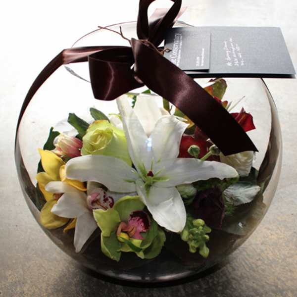 Casablanca lilies, orchids, roses, and snapdragons in a terrarium-style glass vase.