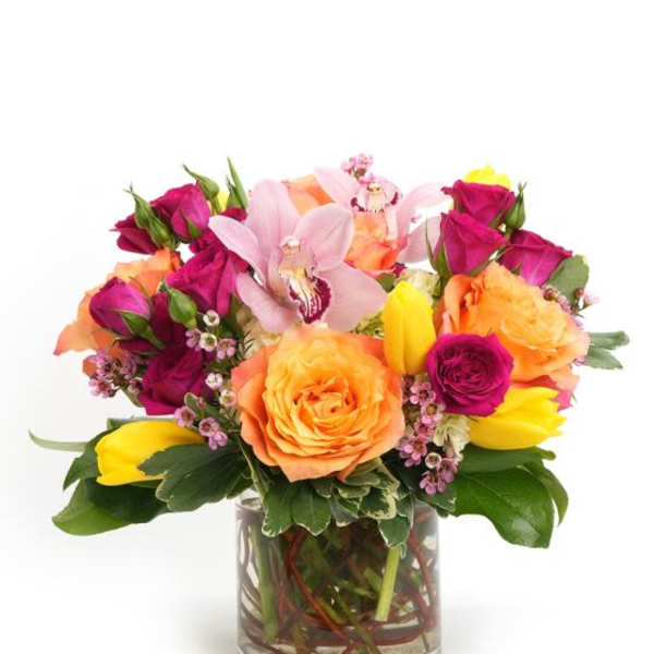 Bright arrangement of orange roses, magenta roses, yellow tulips, and pink orchids in a clear glass vase