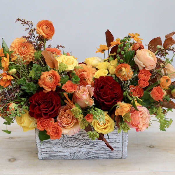 Low autumn-toned arrangement of orange, yellow, and red flowers in a whitewashed wooden box