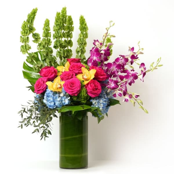 Tall arrangement of pink roses, orchids, and blue hydrangeas in a green-lined glass cylinder vase