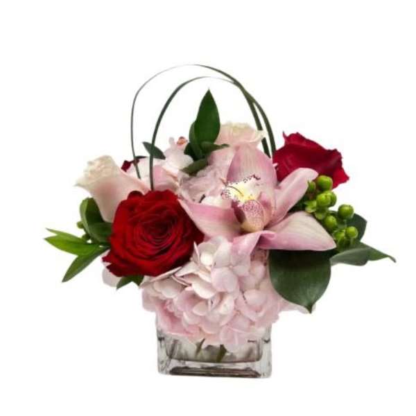 Short arrangement of pink hydrangea with red roses and a pink orchid in a glass cube vase
