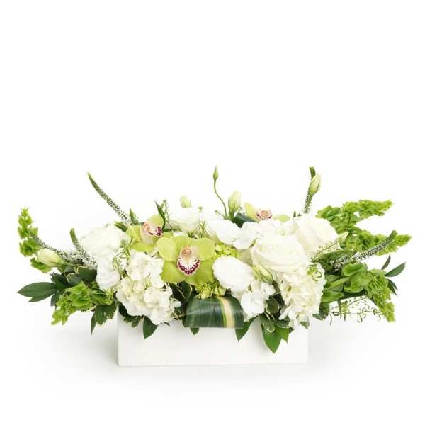 Low white and green floral centerpiece with roses, hydrangeas, and green orchids in a white rectangular container