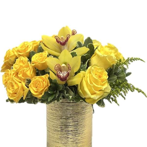 Low arrangement of yellow roses and orchids in a textured gold cylinder vase