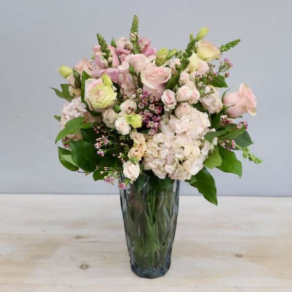 Tall arrangement of pale pink roses and hydrangeas with accent blooms in a faceted glass vase