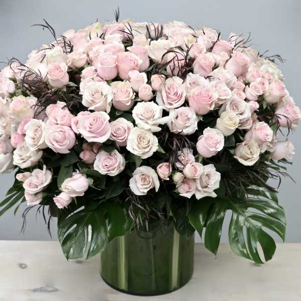 Large dome arrangement of pale pink and white roses in a green glass cylinder vase