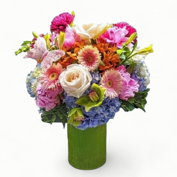 Colorful bouquet of mixed roses, gerberas, and hydrangeas in a green cylinder vase with a decorative butterfly