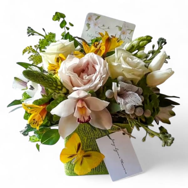 Compact bouquet of white and blush flowers with yellow accents in a green cube vase with a butterfly decoration.
