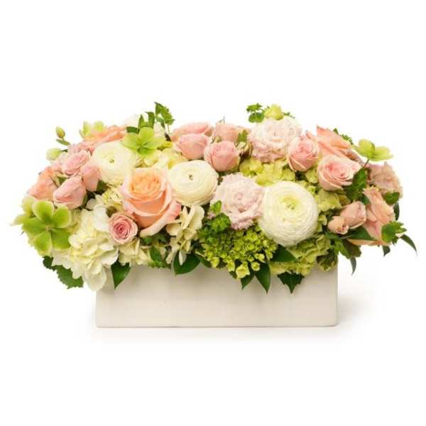 Low pastel arrangement of peach roses, white ranunculus, and green hydrangeas in a white rectangular container