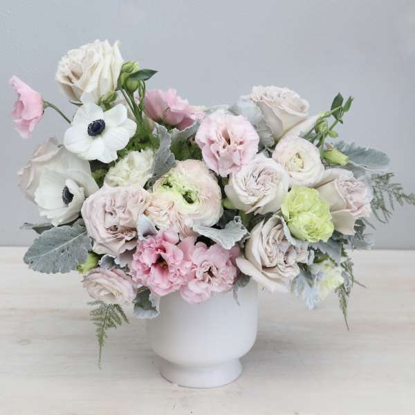 Pastel arrangement of roses, ranunculus, and anemones in a white pedestal vase