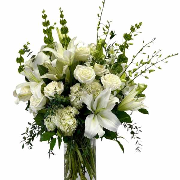 Tall arrangement of white lilies, roses, hydrangeas, and bells of Ireland in a clear glass vase