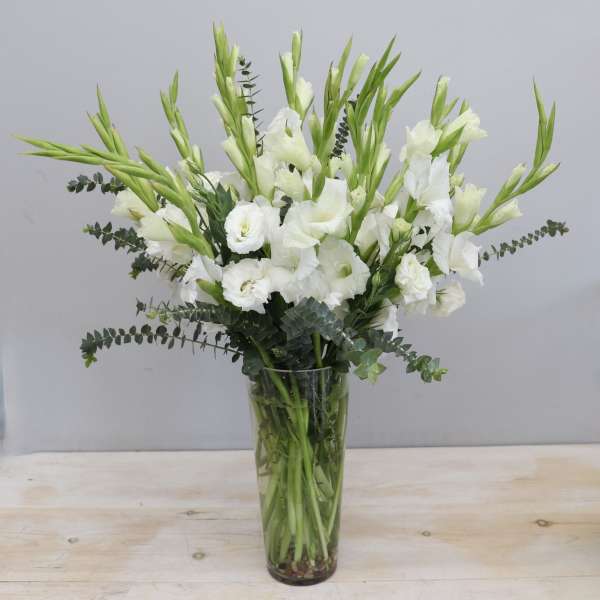 Tall arrangement of white gladiolus and lisianthus in a clear glass vase