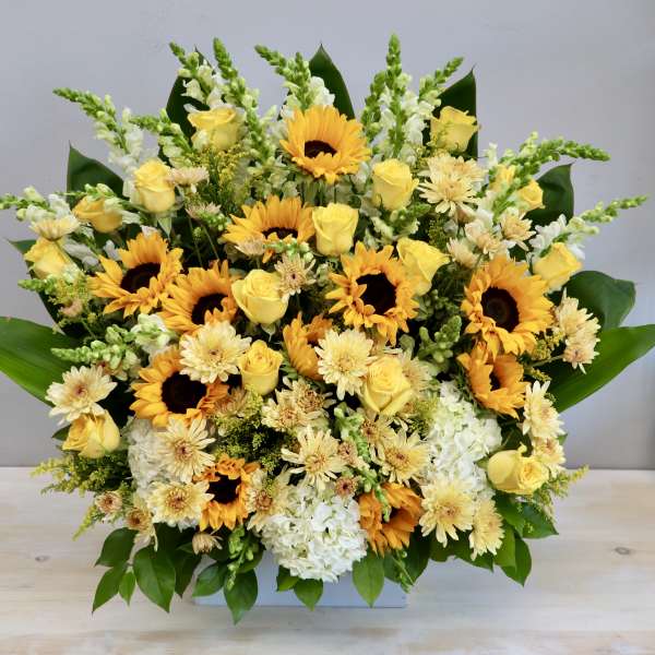 Large arrangement of yellow sunflowers, roses, and white blooms in a low white container