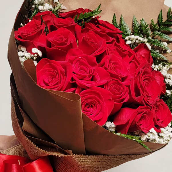 Large bouquet of red roses wrapped in brown paper with white filler flowers and a red ribbon bow.