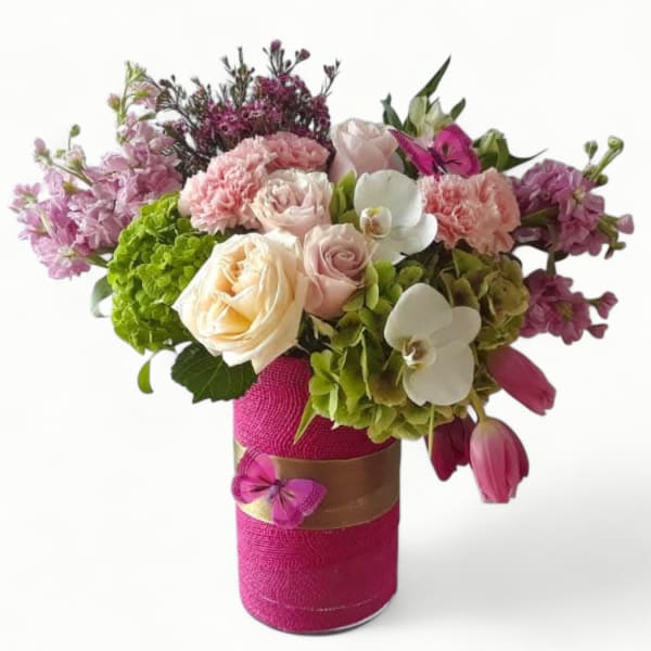 Vase of mixed pink, peach, and white flowers with orchids and tulips in a bright pink wrapped container