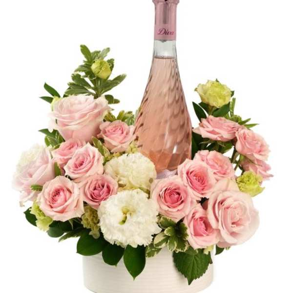 Bottle of pink sparkling wine surrounded by pink roses and white flowers in a white round container