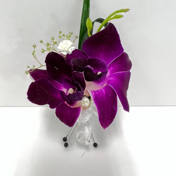 Purple orchid boutonniere with white filler flowers, ribbon, and pins on a white background