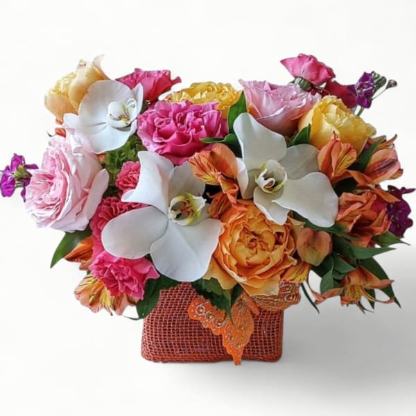 Low arrangement of white orchids, orange and yellow roses, and pink blooms in an orange textured container