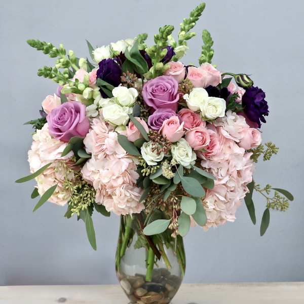 Tall glass vase arrangement with pink hydrangeas, roses, and white and purple accent blooms