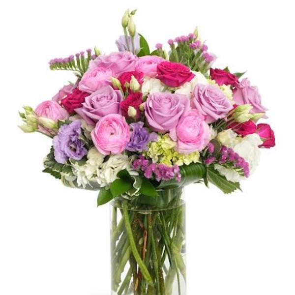 Tall glass vase of pink and lavender roses with mixed pastel flowers in a rounded arrangement