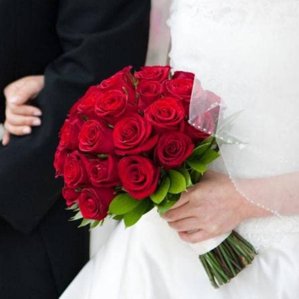 Bridal hand-tied bouquet of clustered red roses held against a white wedding dress