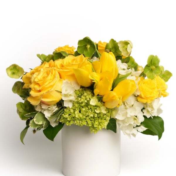 Low yellow and white flower arrangement in a white cylinder vase