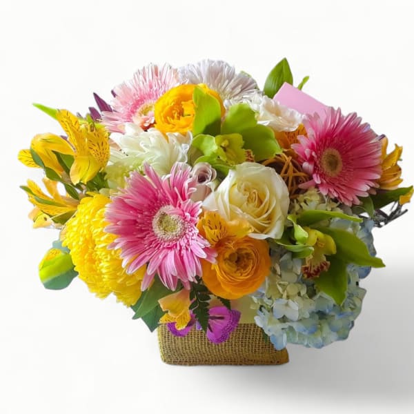 Bright mixed bouquet with pink gerbera daisies, yellow blooms, roses and hydrangea in a square burlap-wrapped vase
