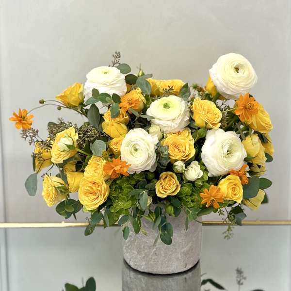 Yellow and white flower arrangement with orange accents in a gray stone pot