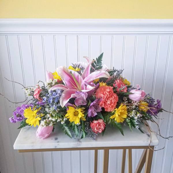 Low centerpiece of pink lilies, carnations, tulips, and yellow daisies in a colorful mixed arrangement