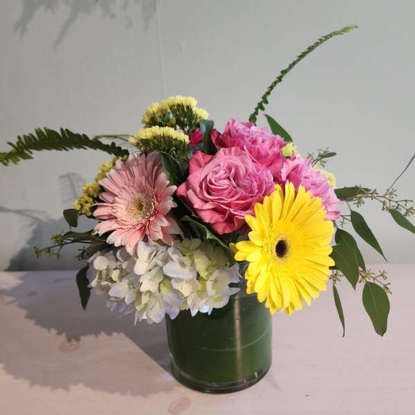 Mixed bouquet of pink roses, gerbera daisies, hydrangea, and yellow gerbera in a leaf-lined glass vase