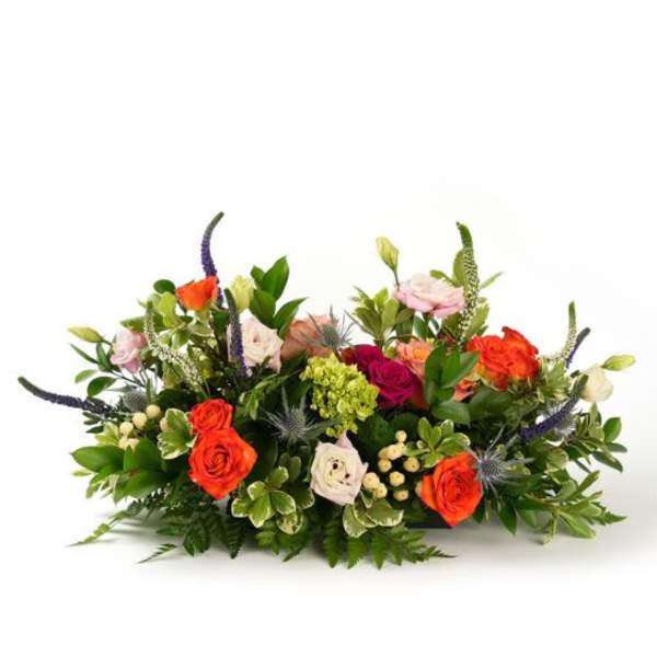 Low centerpiece of bright orange and pink roses with mixed blooms and berries in a horizontal arrangement