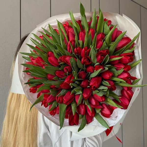 large bouquet of red tulips in white packaging with ribbon