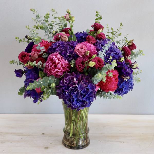Tall arrangement of purple hydrangeas and pink roses in a clear glass vase