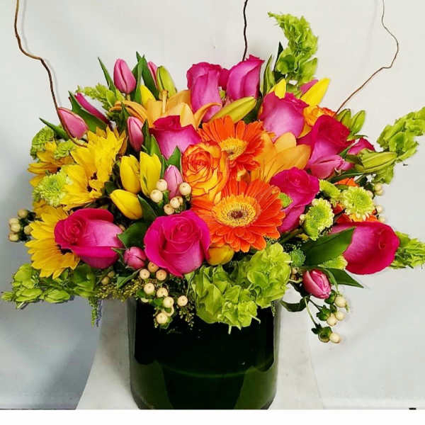 Bright mixed bouquet with pink roses, orange gerberas and yellow blooms in a dark green vase