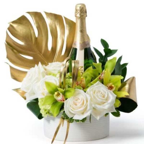 White roses and green orchids arranged around a champagne bottle with gold accents in a white container
