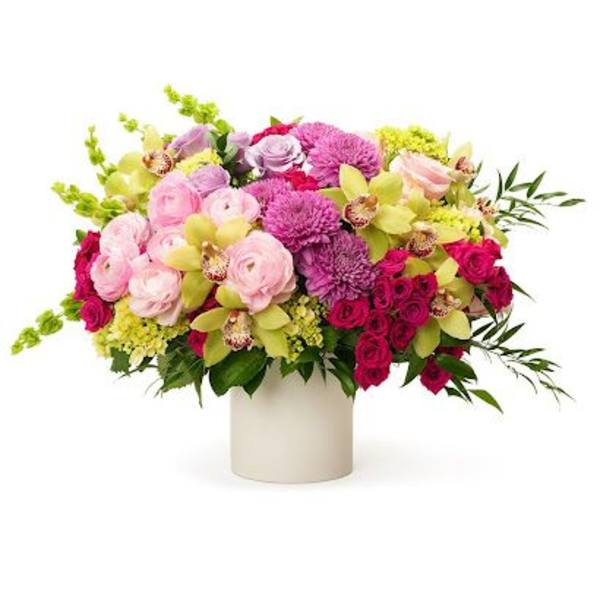Low arrangement of pink roses, purple mums, and green orchids in a white cylinder vase