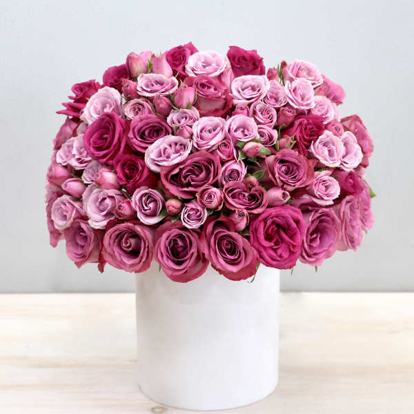 Dome-shaped arrangement of pink and magenta roses in a white cylinder vase