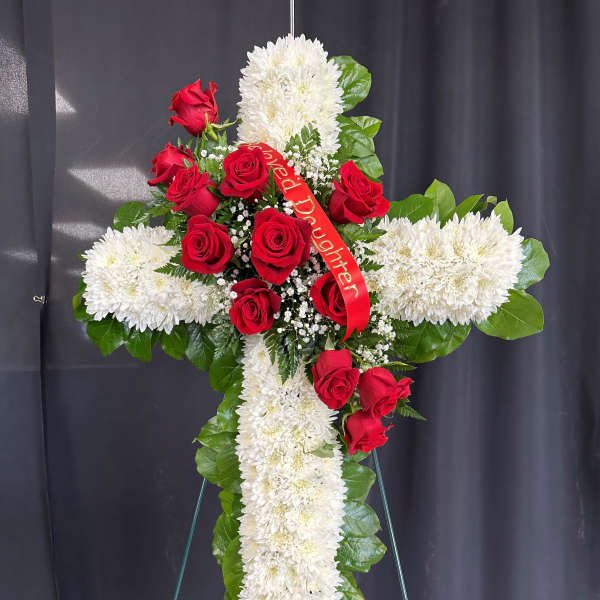 Tall white chrysanthemum cross with red roses and a red memorial ribbon on a metal easel.
