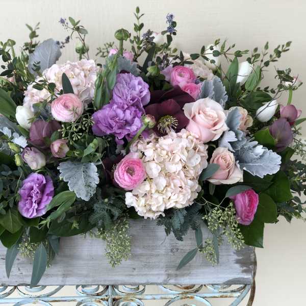 Low pastel arrangement of pink and purple flowers in a rustic rectangular wooden box