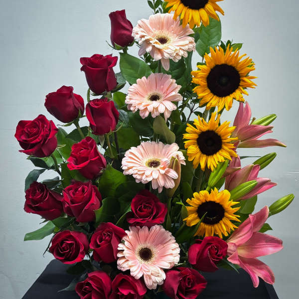 Tall arrangement of red roses, yellow sunflowers, pink gerbera daisies, and pink lilies