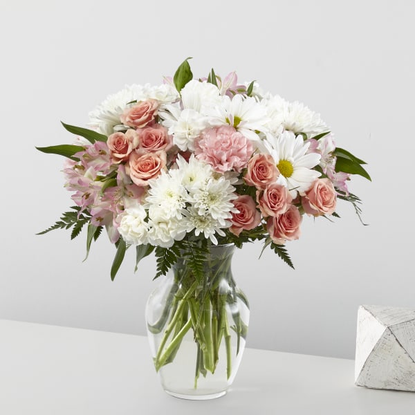 Mixed bouquet of white daisies and mums with peach roses in a clear glass vase
